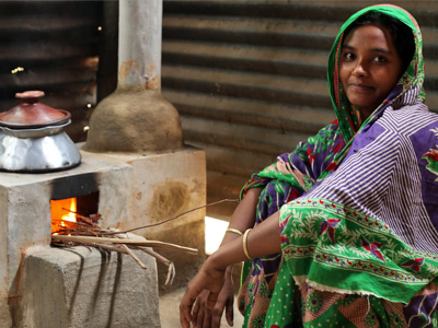 A woman in Bangladesh sits with her Bondhu Chula stove – a clean cooking appliance provided by organisation ClimateCare, who mark-making* support.