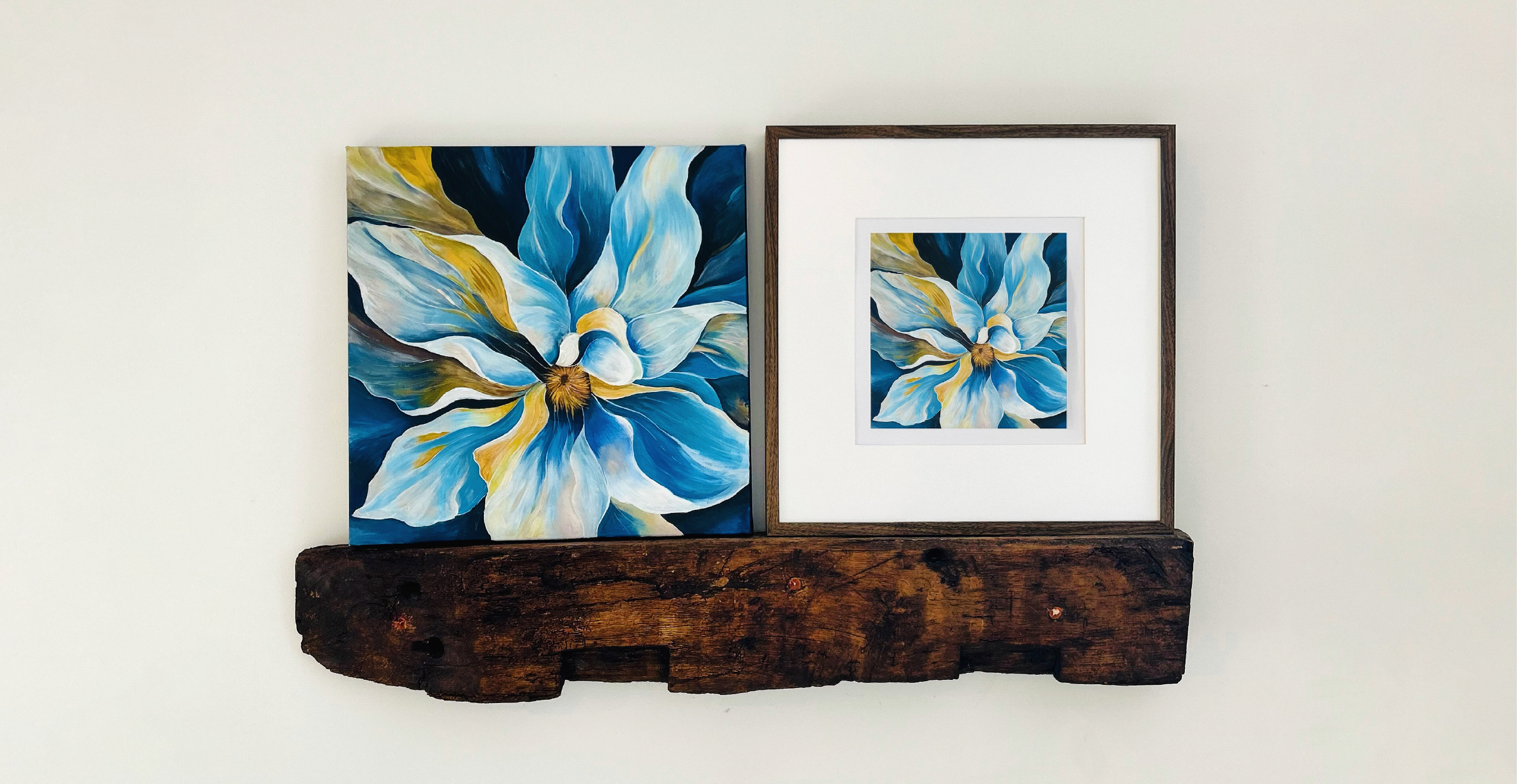 A vibrant painting of a large blue and white flower with golden yellow accents, displayed side by side in two formats: a canvas on the left and a framed print on the right. Both artworks are mounted on a rustic wooden shelf against a plain white wall, showcasing the intricate brushwork and rich colors of the design.